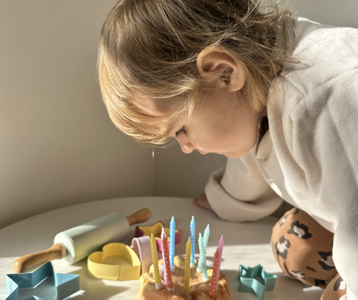 The girl is blowing out candles on the playdough cake. The girl is blowing out candles on the playdough cake.